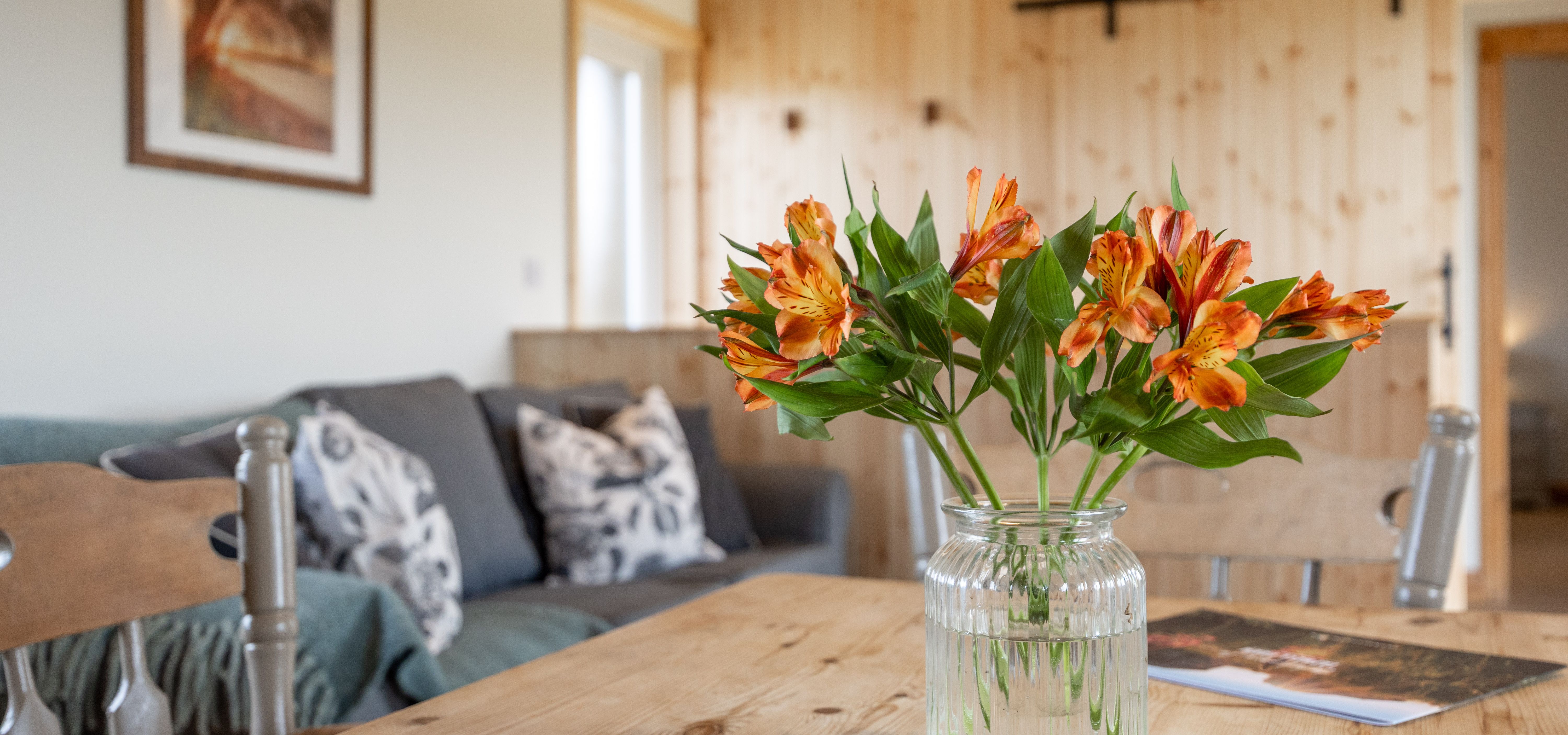 Orange flowers in a glass jar on a wooden dining table in a cosy lodge living area