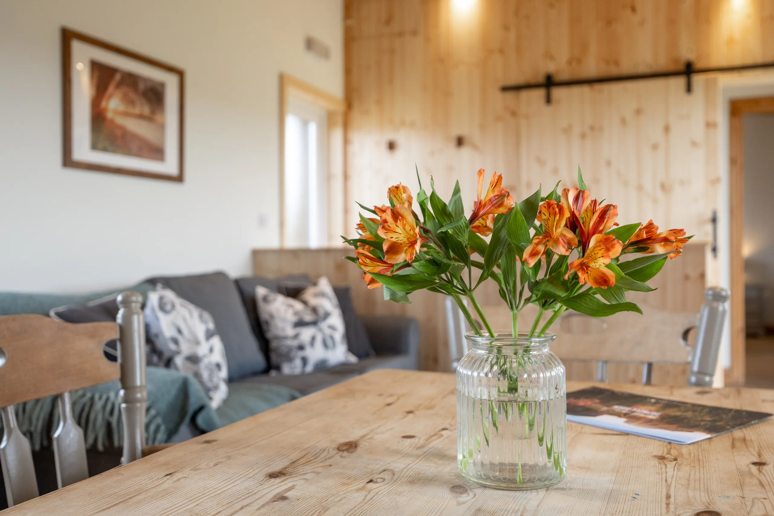 Orange flowers in a glass jar on a wooden dining table in a cosy lodge living area