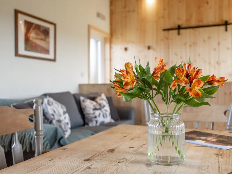 Orange flowers in a glass jar on a wooden dining table in a cosy lodge living area