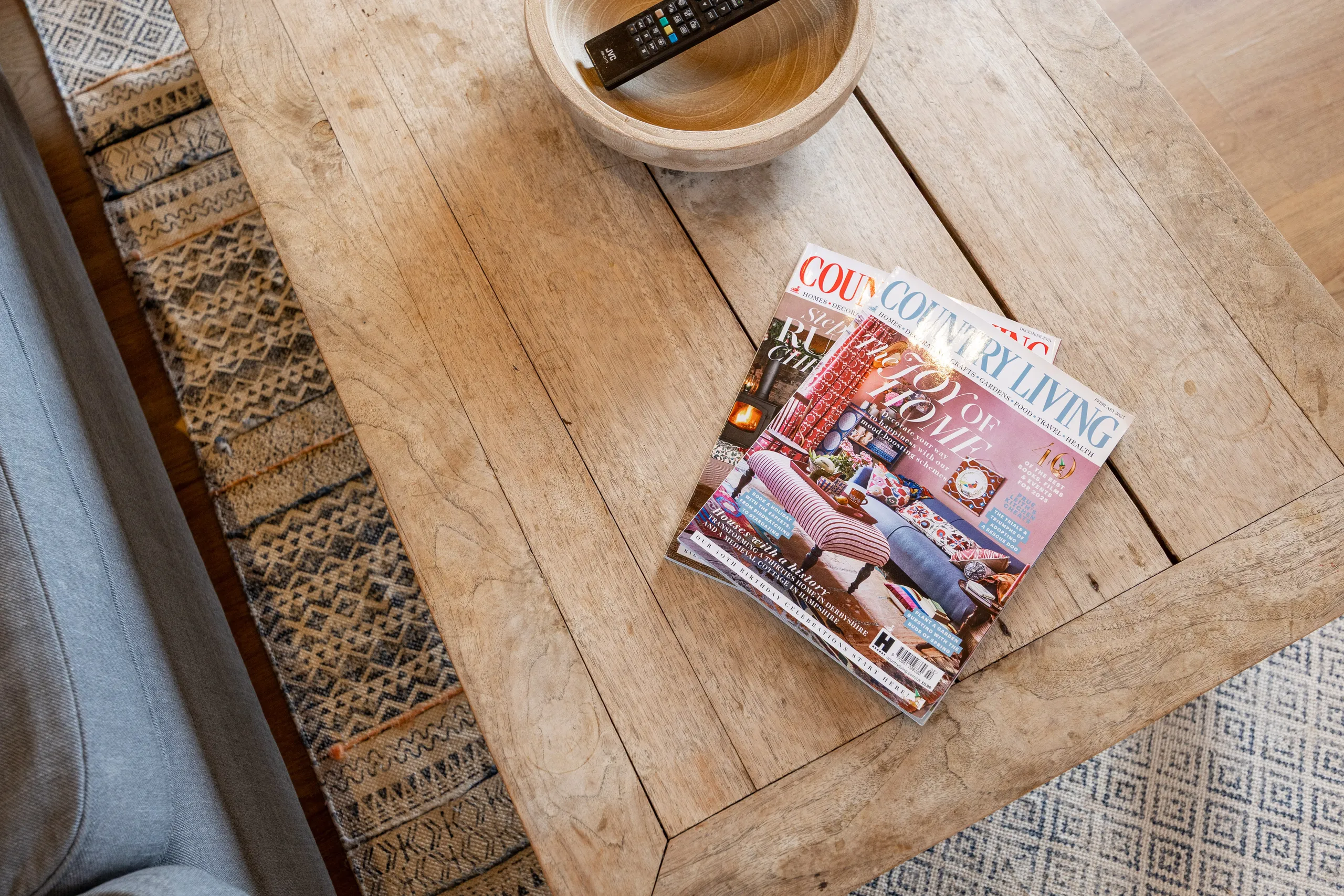 Wooden coffee table with a magazine and TV remote in a bowl