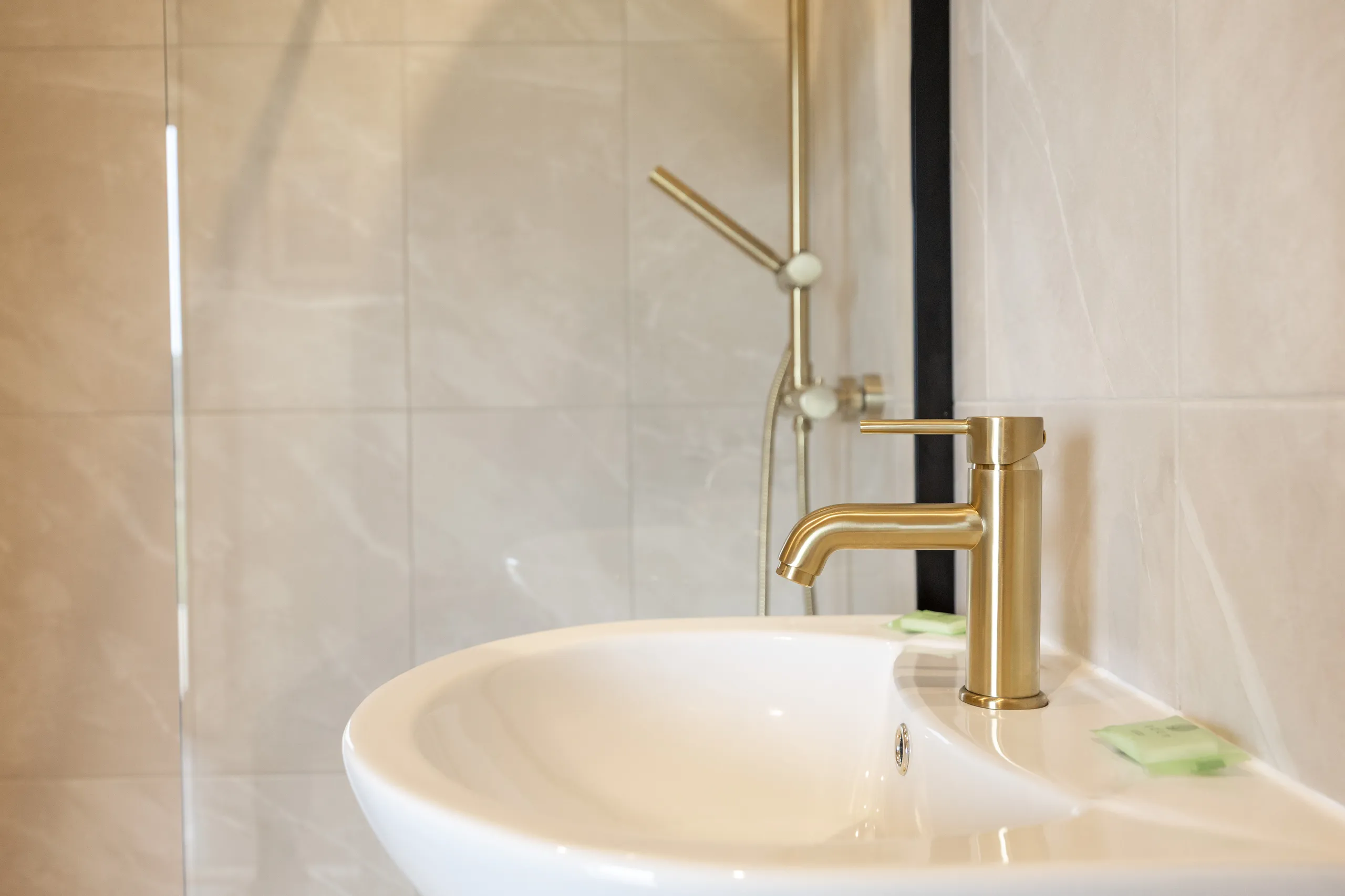 Modern bathroom sink with brass tap and shower in tiled enclosure