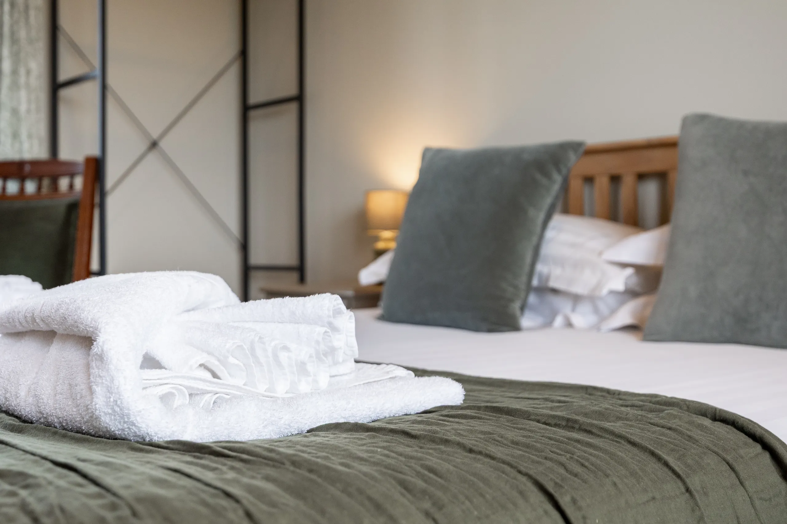Folded white towels on a bed with grey cushions and a wooden headboard in a cosy bedroom
