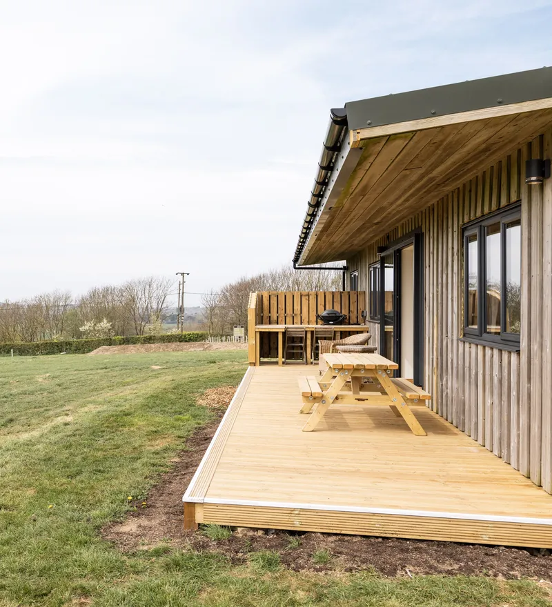 Wooden lodge with decking and picnic table overlooking rolling countryside