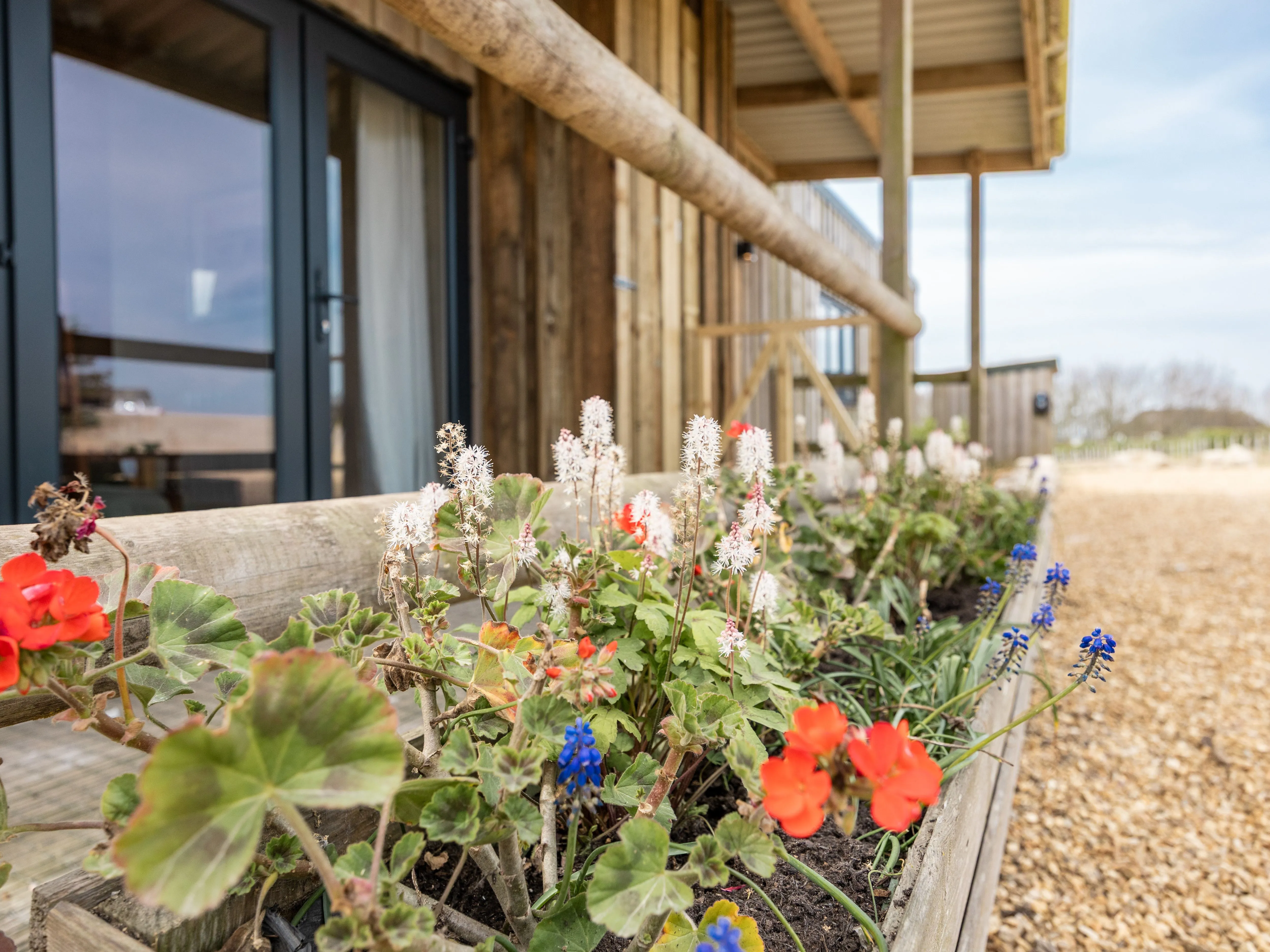 Flower-filled wooden planter beside a timber lodge with glass doors and balcony