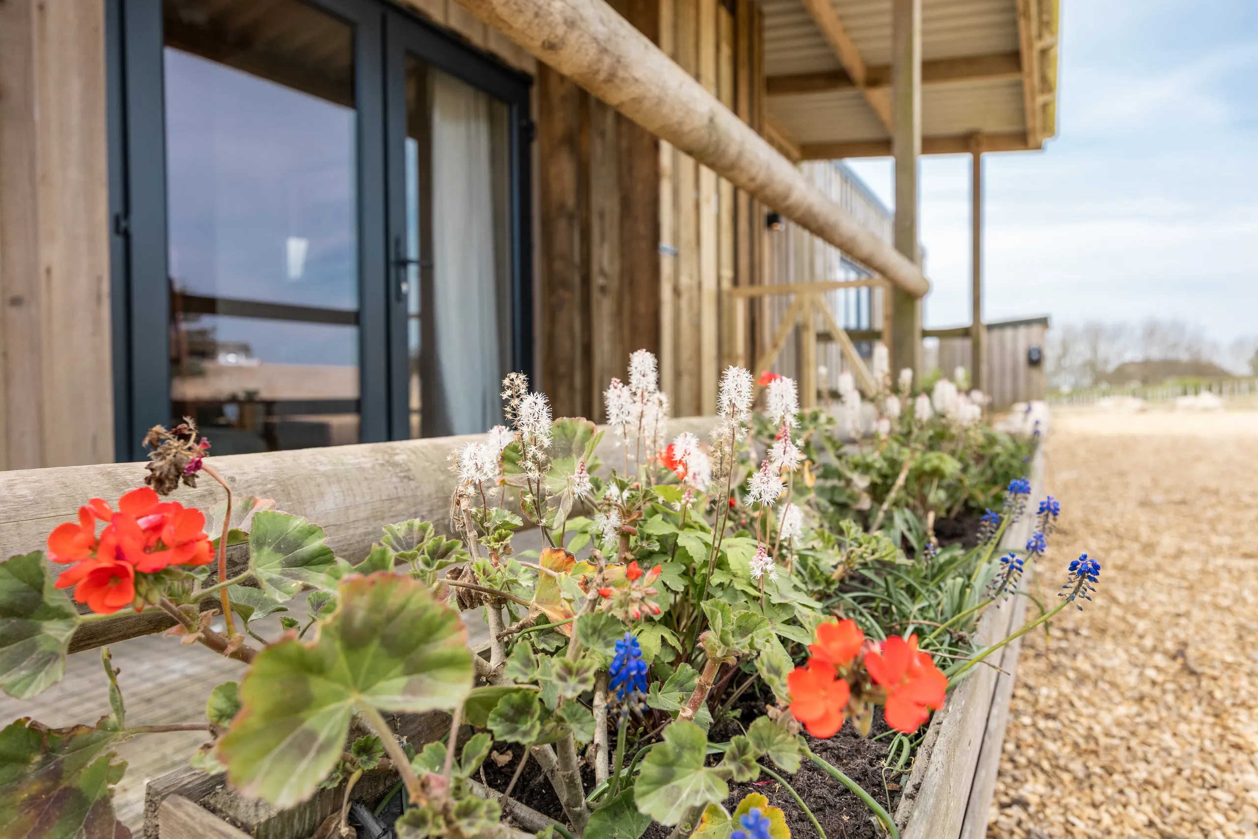 Flower-filled wooden planter beside a timber lodge with glass doors and balcony