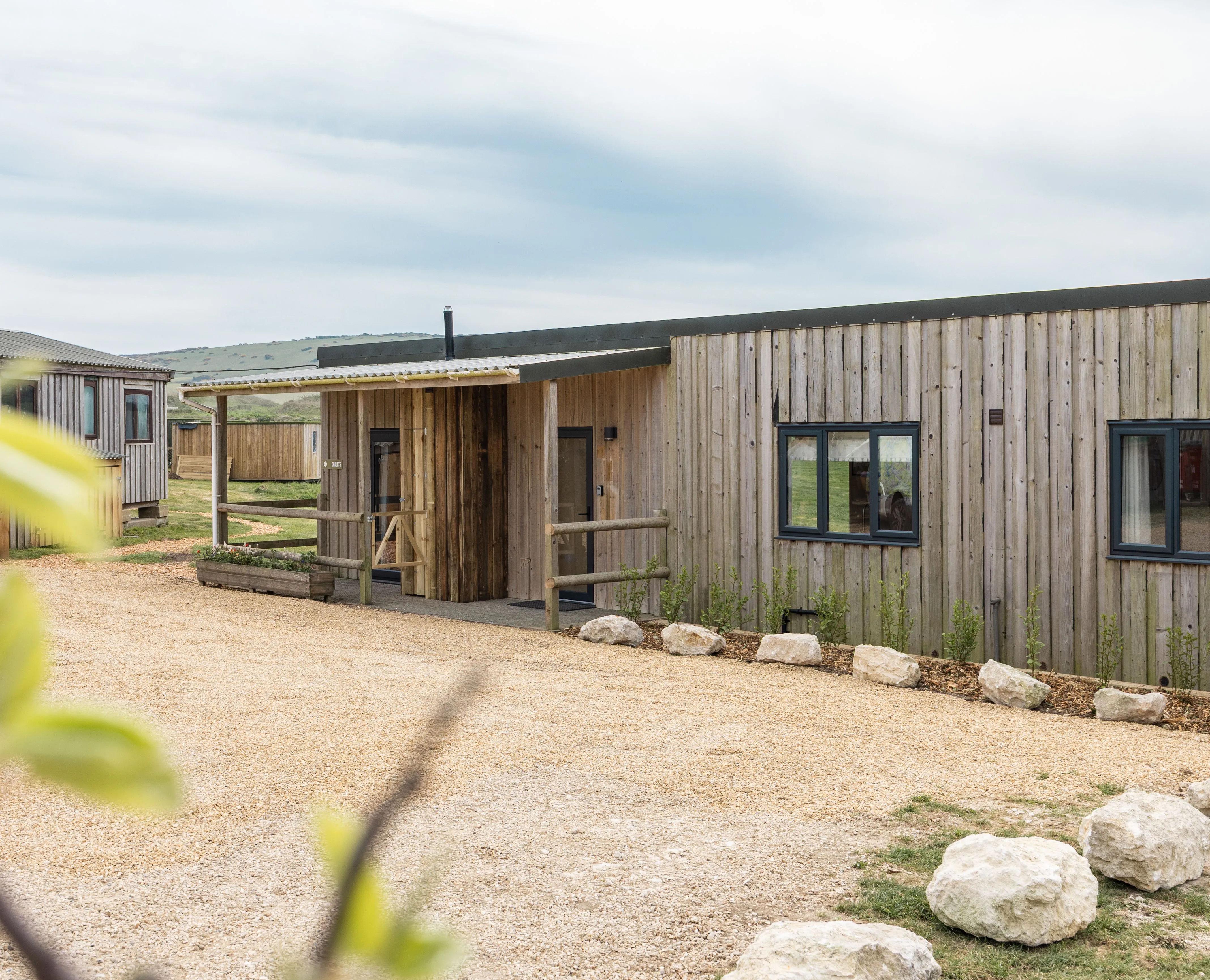 Exterior of a modern timber-clad lodge with gravel driveway and countryside views