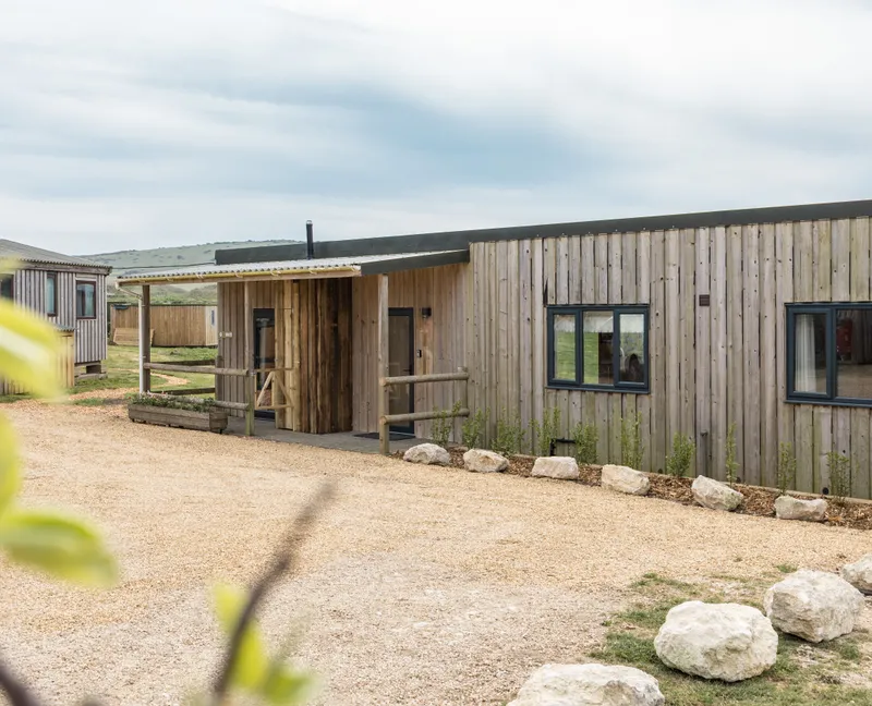 Exterior of a modern timber-clad lodge with gravel driveway and countryside views