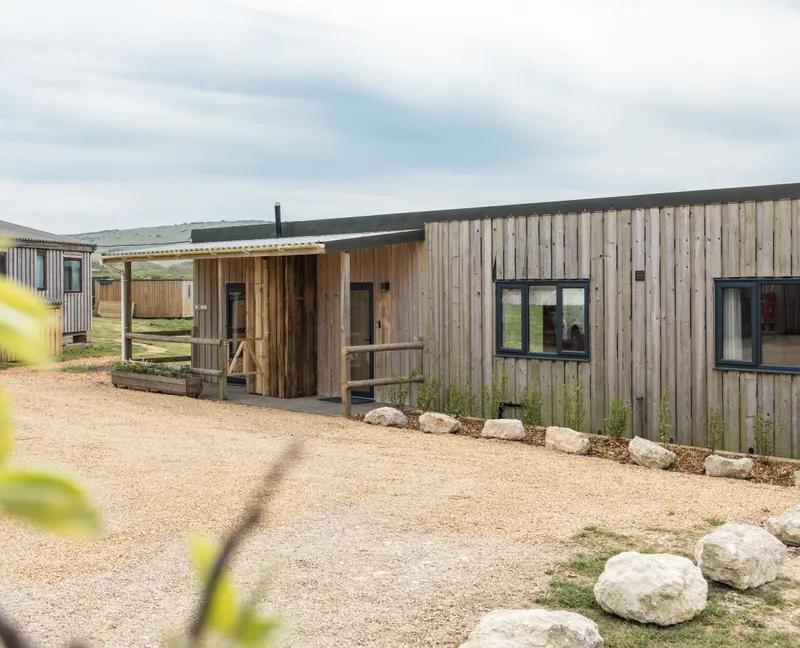 Exterior of a modern timber-clad lodge with gravel driveway and countryside views