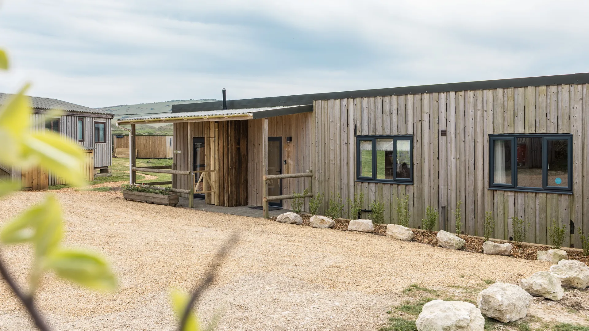 Exterior of a modern timber-clad lodge with gravel driveway and countryside views