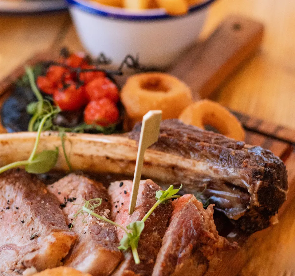 Steak and chips served on a wooden board with onion rings and roasted vine tomatoes