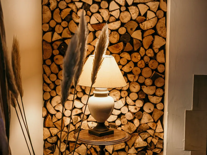 Table lamp glowing in front of a stacked log wall with pampas grass stems