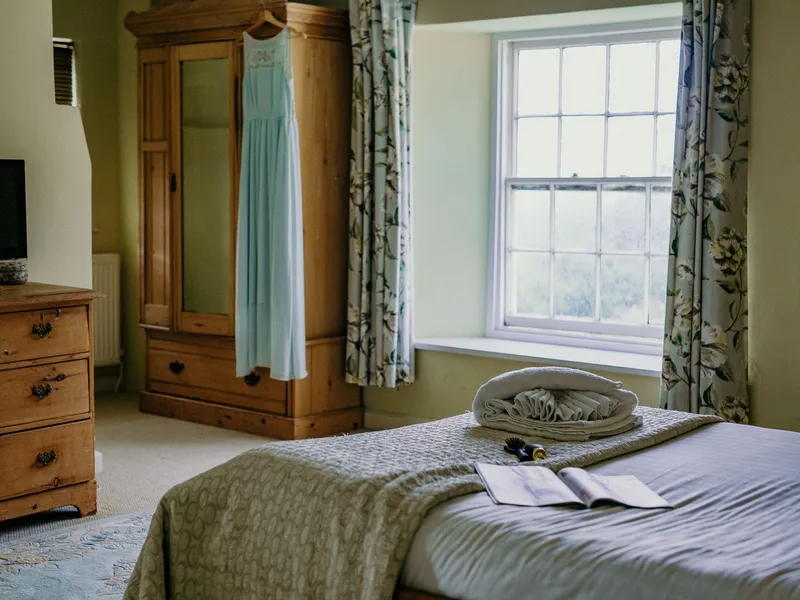 Cosy bedroom with wooden wardrobe, floral curtains and neatly folded towels on the bed