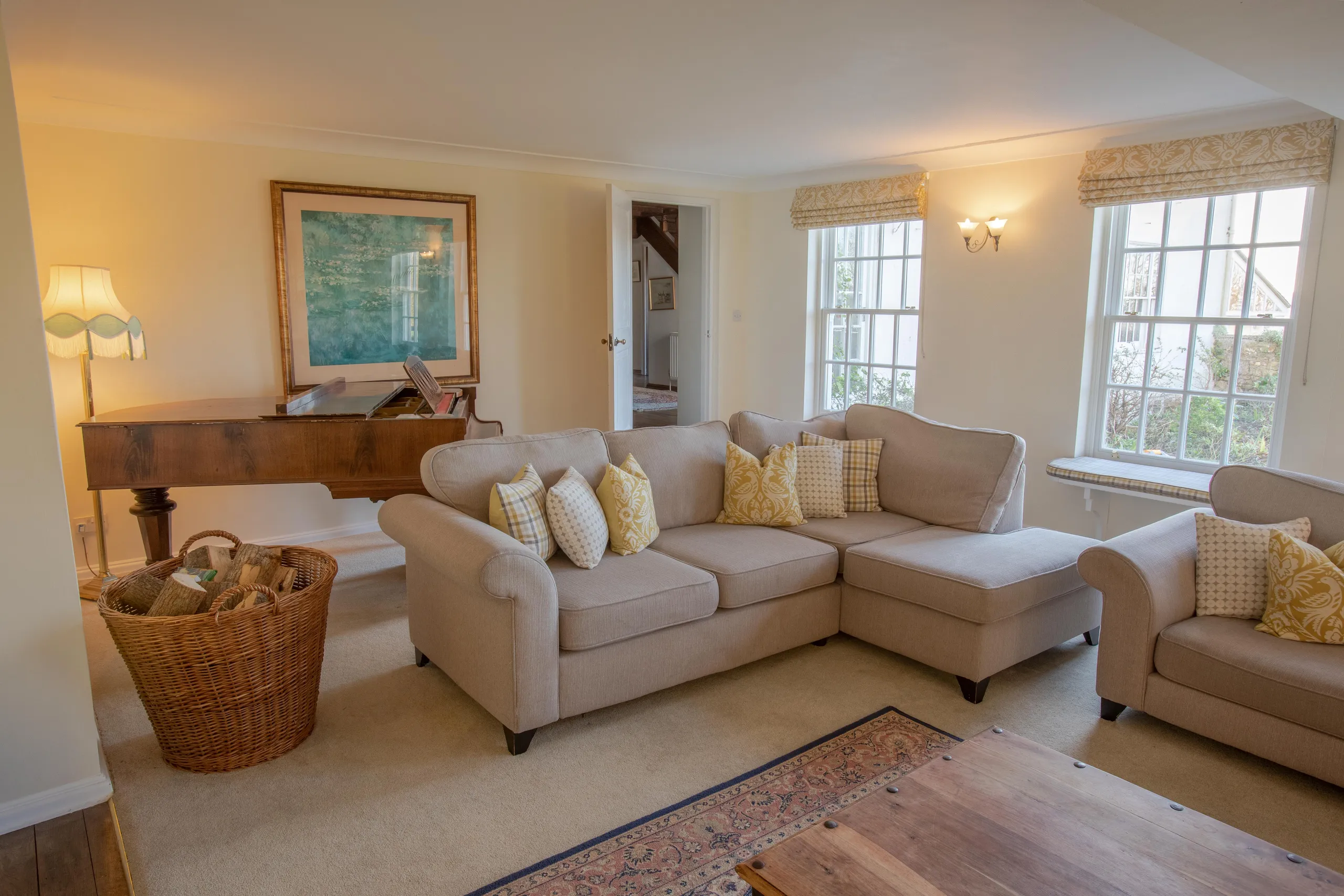 Cosy living room with beige corner sofa, armchair, grand piano and large windows