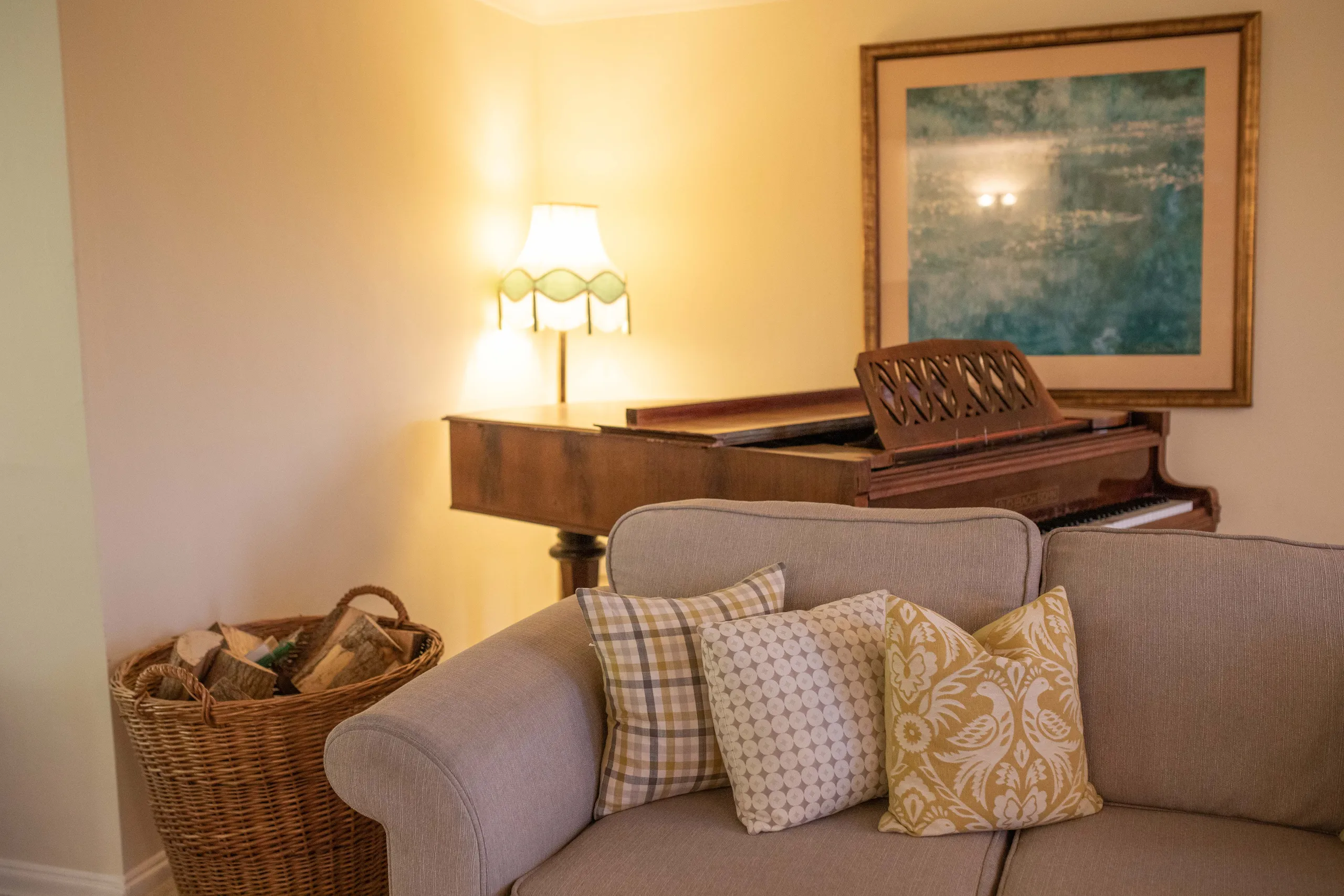 Cosy sitting room with a grand piano, table lamp and sofa with patterned cushions