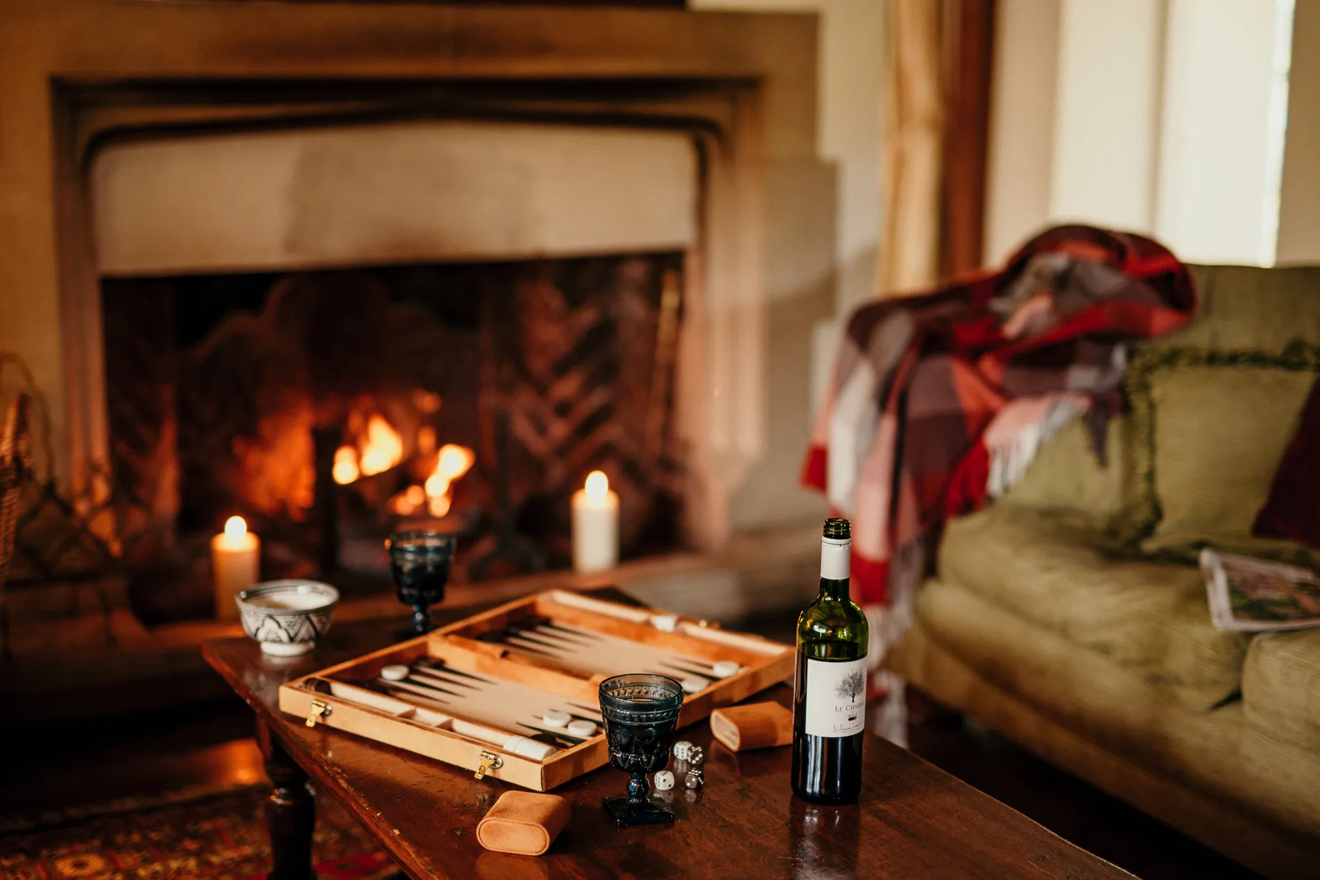 Cosy living room with a lit fireplace, candles, a backgammon set and a bottle of wine on a wooden table