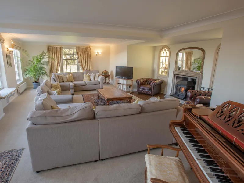 Spacious lounge with grey sofas, wood-burning stove, television and upright piano