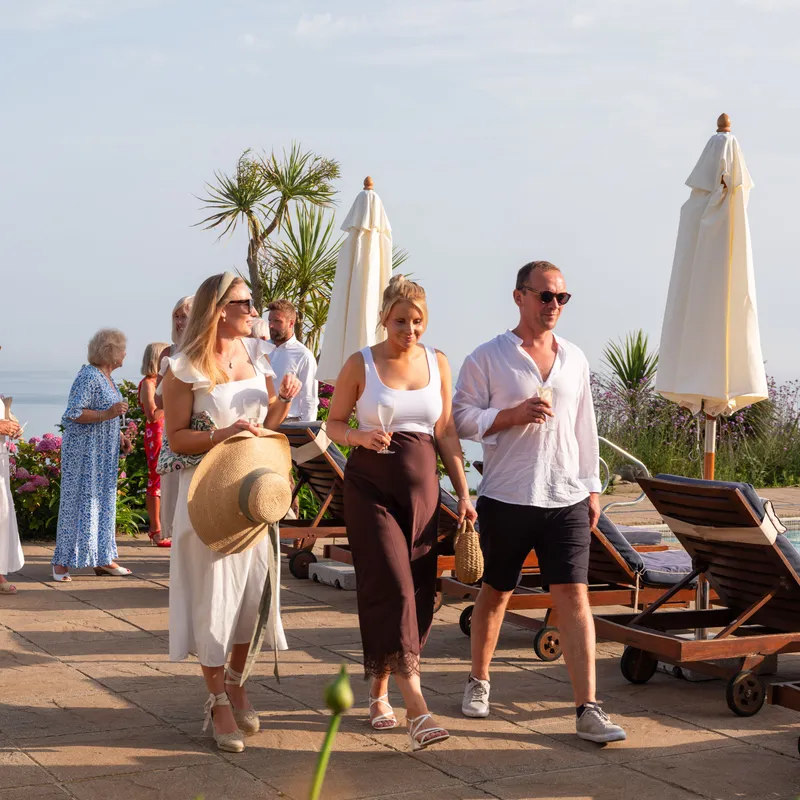 Guests enjoying drinks beside a seaside swimming pool with loungers and parasols