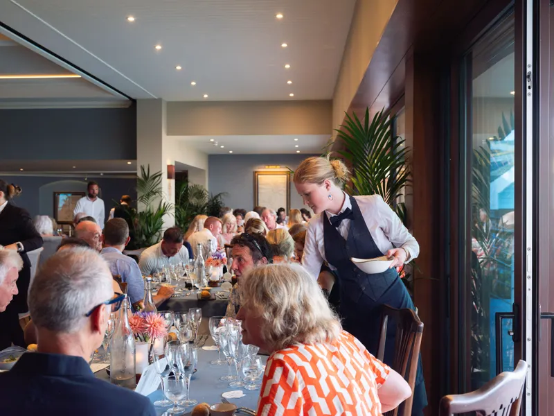 Waitress serving guests at a long table during an elegant restaurant gathering.
