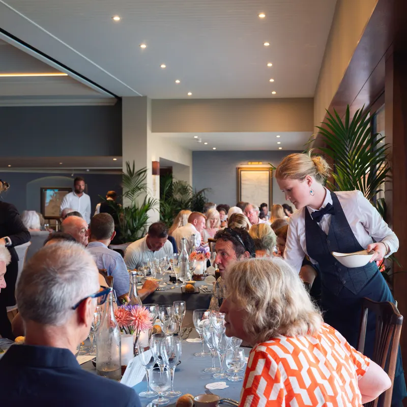 Waitress serving guests at a long table during an elegant restaurant gathering.
