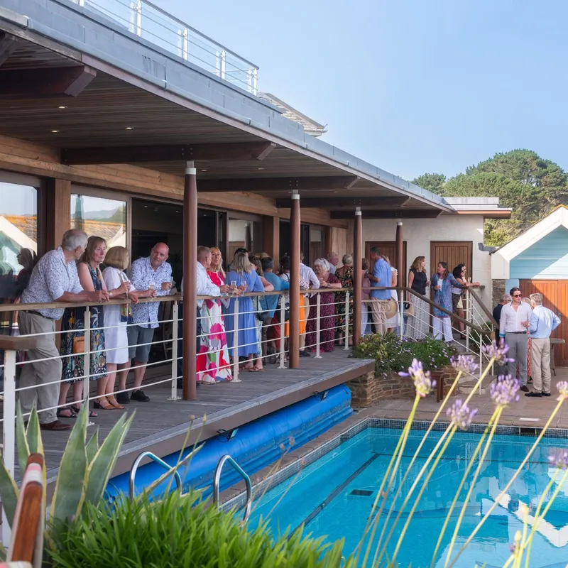 Guests gathered on a wooden terrace beside a swimming pool at a modern countryside home.