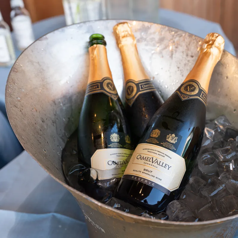Three bottles of Camel Valley sparkling wine chilling in ice inside a metal drinks bucket.