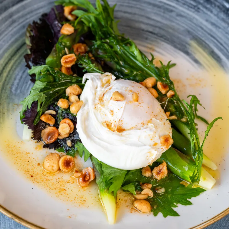 Poached egg atop a leafy green salad with hazelnuts and dressing in a ceramic bowl
