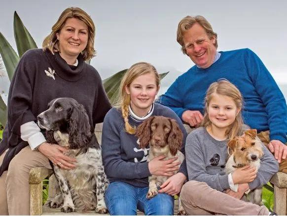 Family of four sitting outdoors with three dogs in a garden