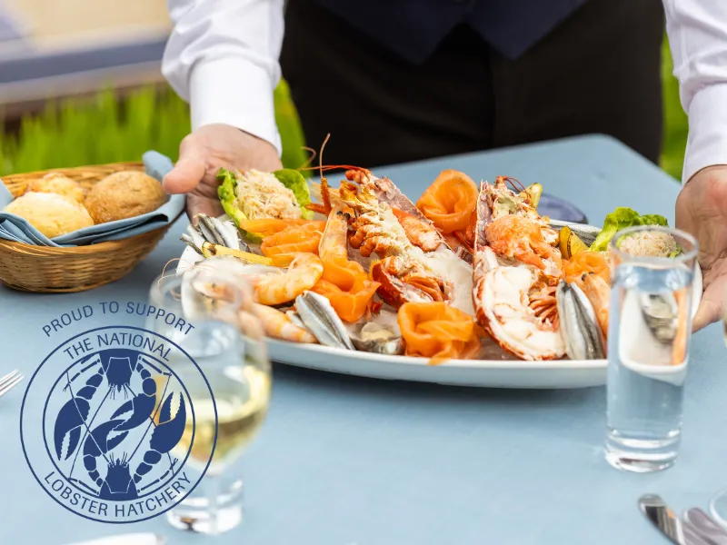 Waiter serving a platter of lobster, salmon, prawns and mussels at an outdoor table