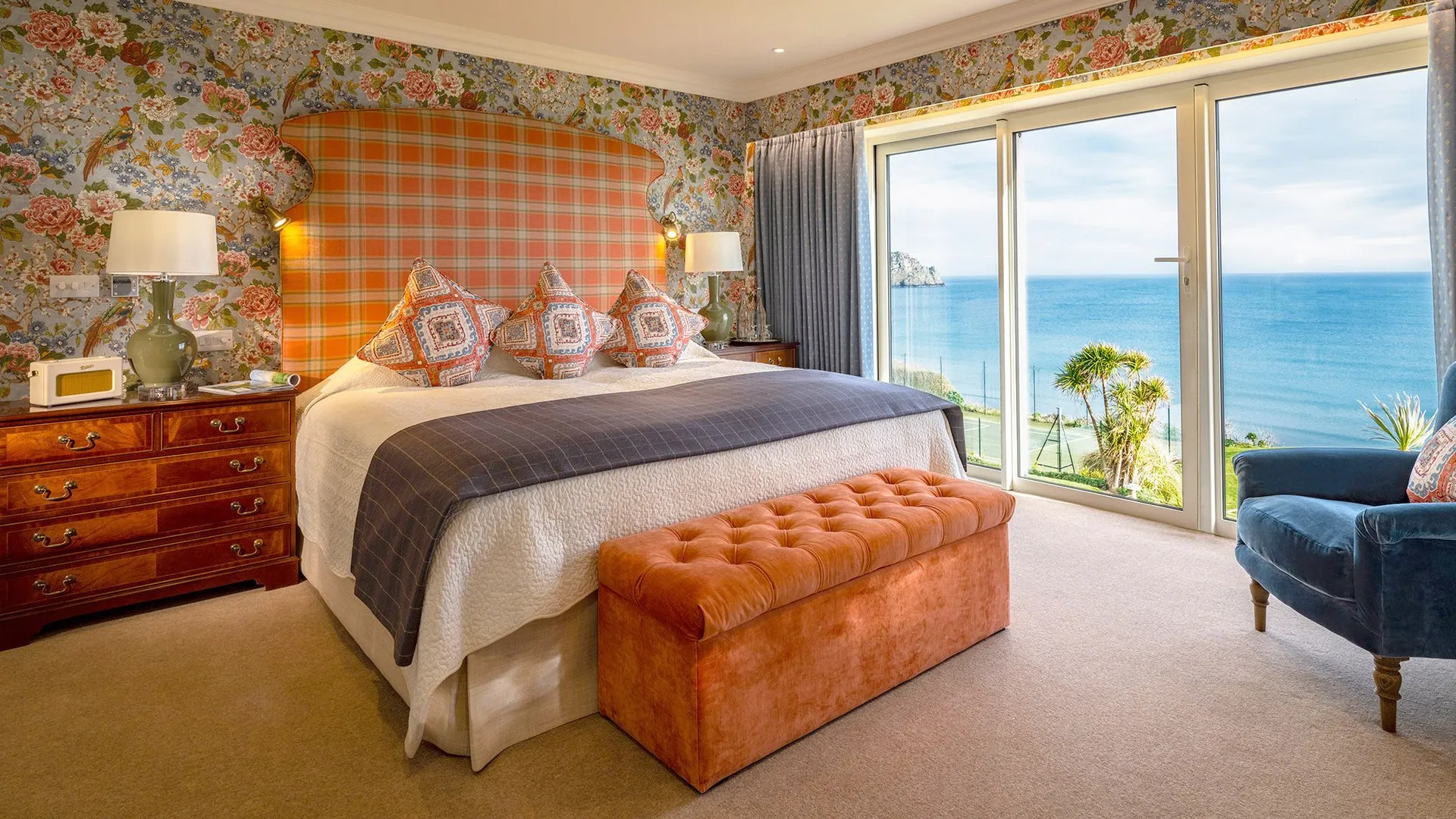 Elegant hotel suite bedroom with floral wallpaper, a large bed and floor-to-ceiling doors opening to sea views