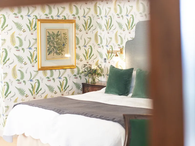 Elegant bedroom with botanical wallpaper, a white bed, green cushions and a framed print