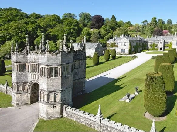 Aerial view of a grand historic stone manor with formal gardens and ornate gatehouse in Cornwall