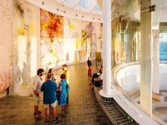 Visitors in a bright contemporary gallery with large abstract wall artworks and sea views.