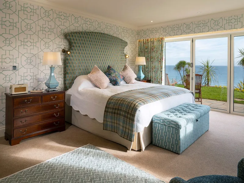 Elegant suite bedroom with patterned wallpaper, a large bed, and sliding glass doors opening to a sea-view terrace.