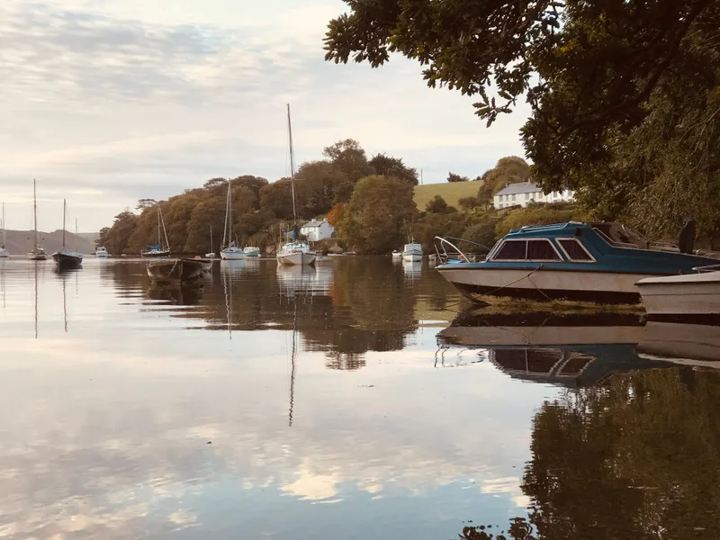 Boats moored on calm water beside tree-lined countryside and white cottages