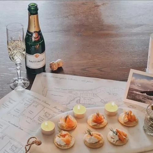 Champagne, smoked salmon canapés and candles arranged over printed plans on a wooden table