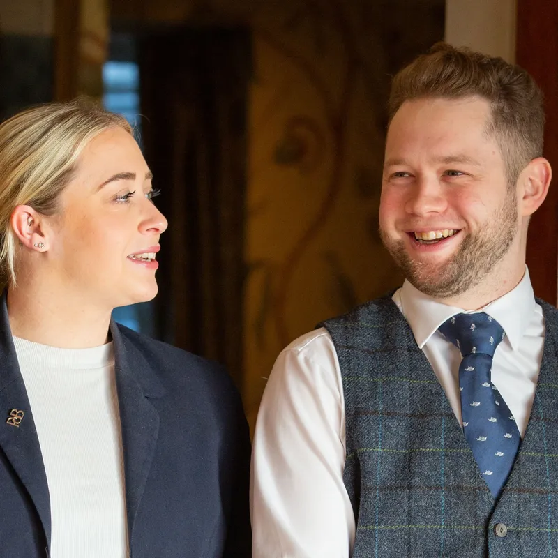Two smartly dressed staff members smiling and talking indoors