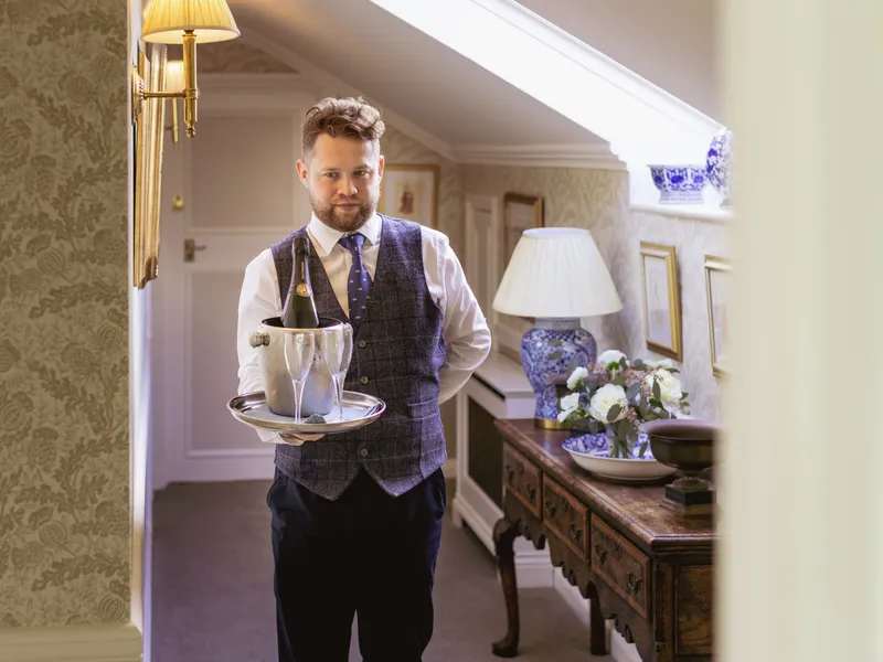 Man in a waistcoat holding a tray with champagne and glasses in an elegant hallway