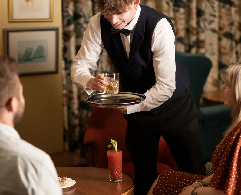 Waiter in a waistcoat serving a drink to guests in a lounge