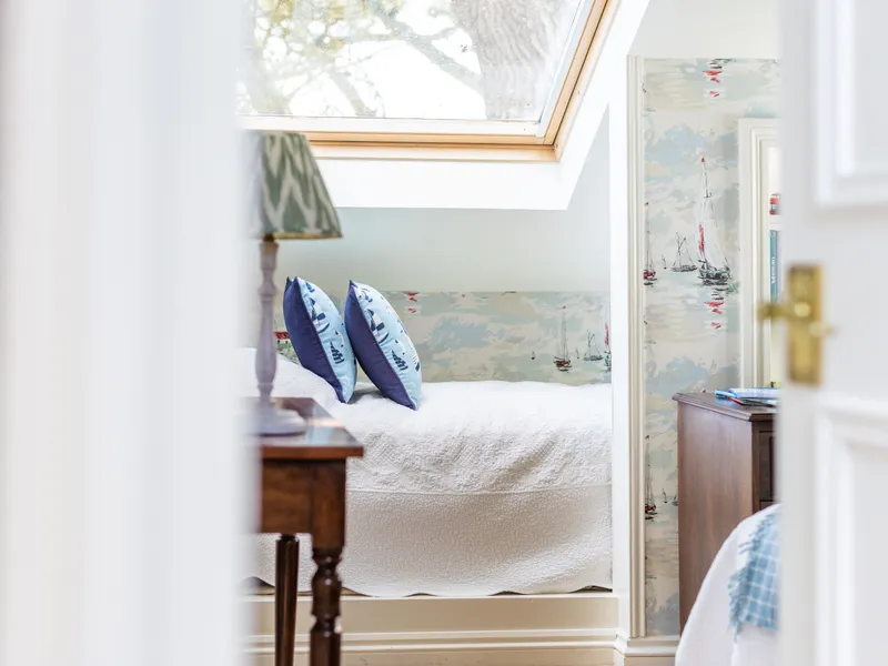 Bright attic bedroom with a single bed beneath a skylight, nautical wallpaper and blue patterned cushions
