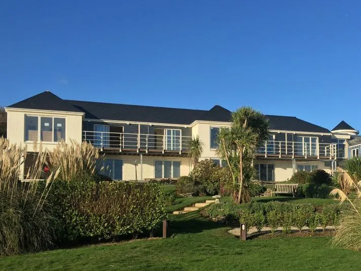 Modern two-storey building with balconies overlooking a landscaped garden beneath a clear blue sky.
