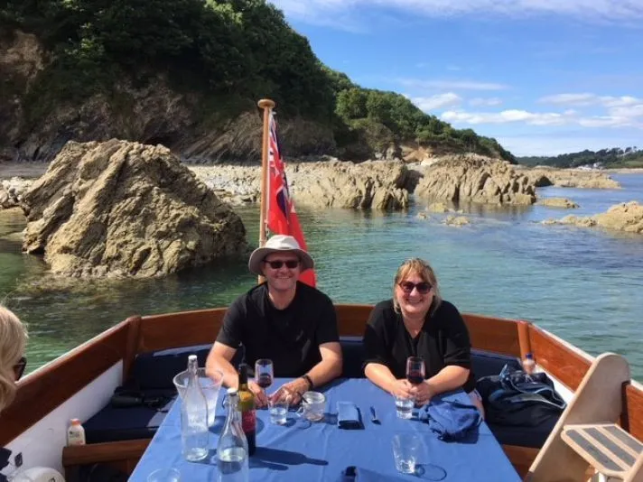 Two people seated at a table aboard a boat in a rocky coastal cove