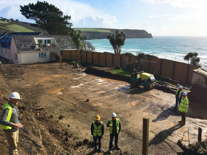 Construction workers in high-visibility vests and hard hats survey a coastal building site overlooking the sea.