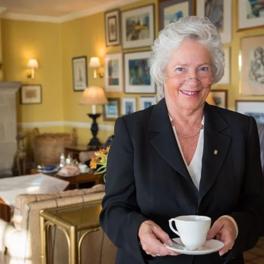 Smiling older woman holding a cup and saucer in a warmly lit sitting room