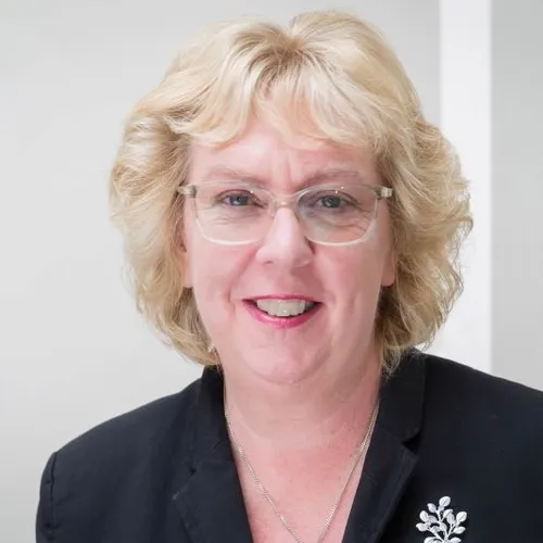 Smiling blonde woman wearing glasses and a dark blazer