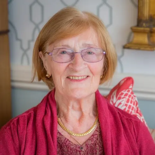Smiling older woman with glasses wearing a red cardigan and gold necklace