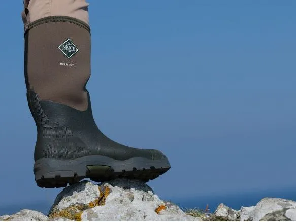 Close-up of a brown and black Muck Boot standing on a rocky outcrop against a blue sky