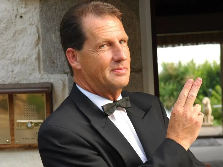 Man in a black dinner jacket and bow tie posing with two fingers raised