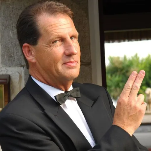Man in a black dinner jacket and bow tie posing with two fingers raised