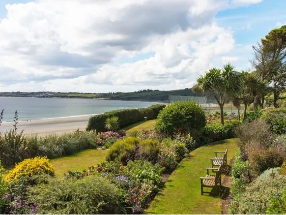 Landscaped coastal garden with wooden benches overlooking a sandy beach and calm bay