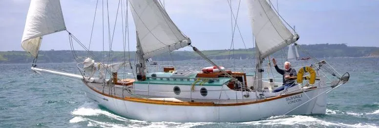 White two-masted sailing yacht underway at sea, with a person waving from the stern
